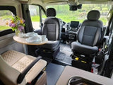 Step inside this RV rental! A bright camper van interior with swiveling front seats, dining table, and compact kitchen.