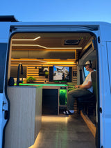 Mobile gaming setup in a modern RV rental. A person plays video games in a custom van with LED lighting and a full kitchen.