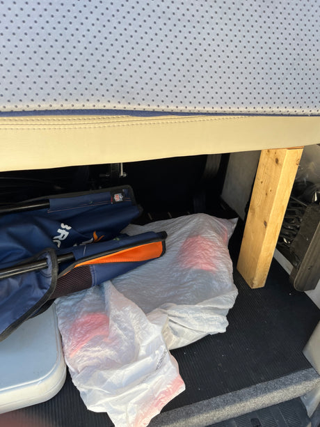 RV rental interior: Under-seat storage packed with a cooler, NFL chair, plastic bags, and a wood support.