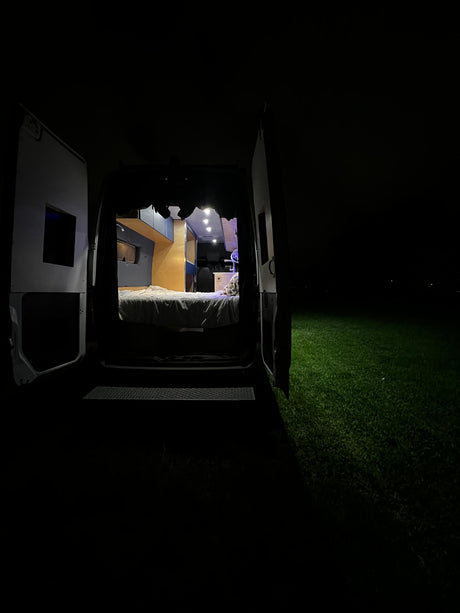 Cozy rv rental camper van interior at night with open doors, illuminating grass outside.