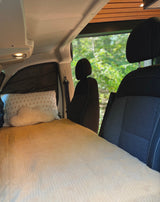 Cozy RV rental interior with a made bed, pillows, ceiling light, and a scenic nature view outside.