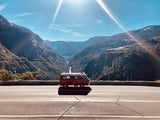 Stunning mountain valley view with a red camper van on the road. Plan your next scenic RV rental adventure through breathtaking landscapes.