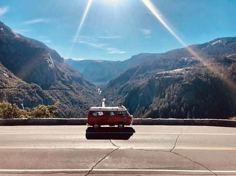 Stunning mountain valley view with a red camper van on the road. Plan your next scenic RV rental adventure through breathtaking landscapes.