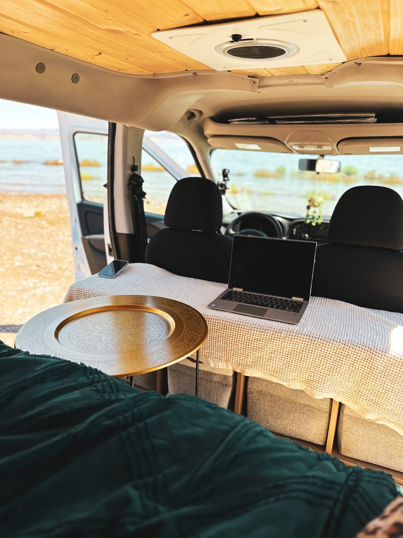 Enjoy remote work from this inviting rv rental. Van interior features a laptop, golden tray, and scenic water view.