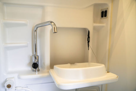 RV rental: Compact white wet bath with a chrome faucet and a hinged, space-saving sink.