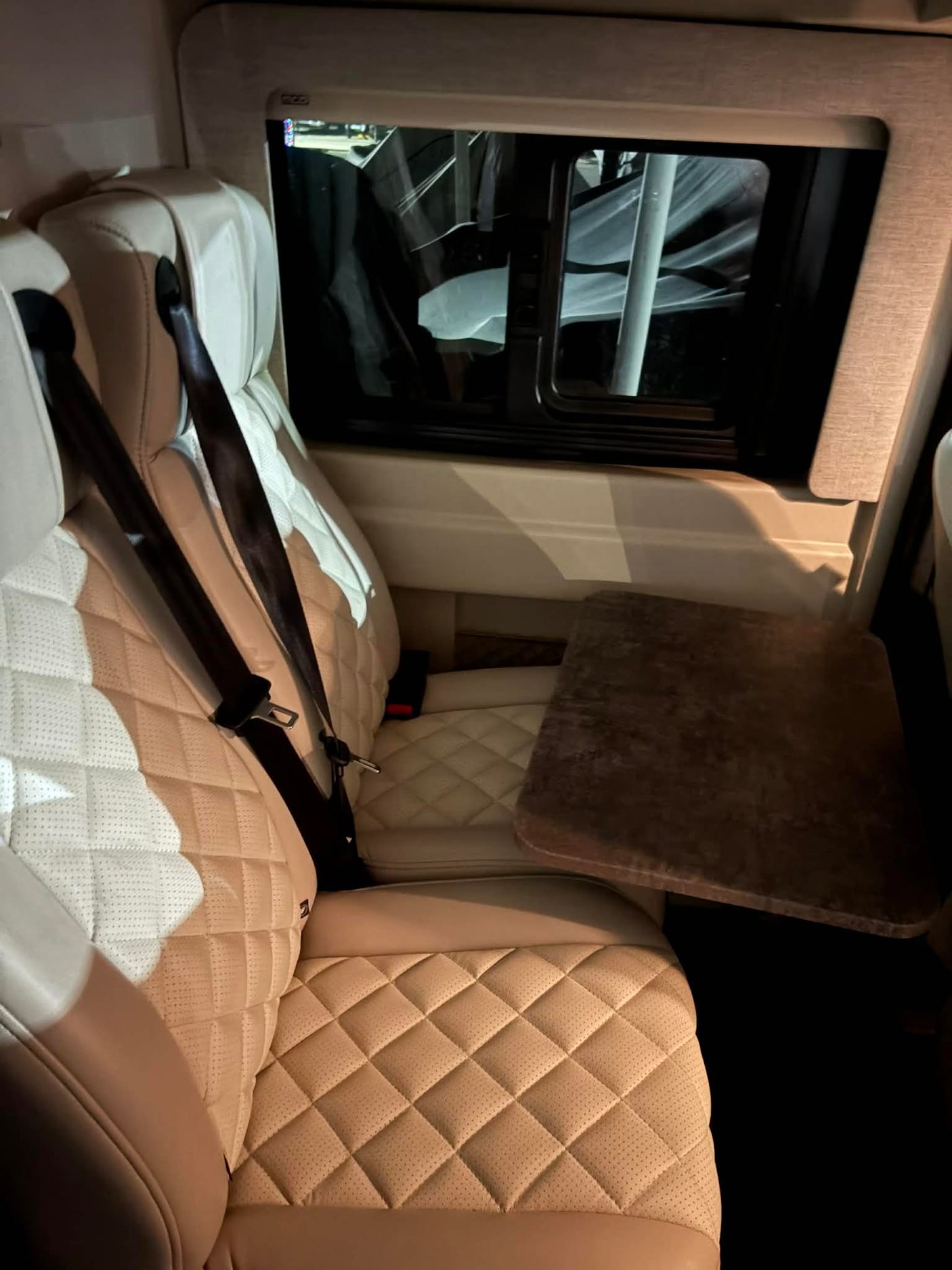 Inside an RV rental, showing plush quilted seats with seatbelts, a side table, and a window view.