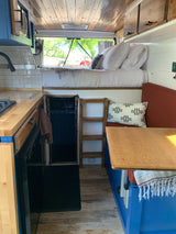 Inside a stylish RV rental! This custom van features a kitchen, raised bed, and dining nook.