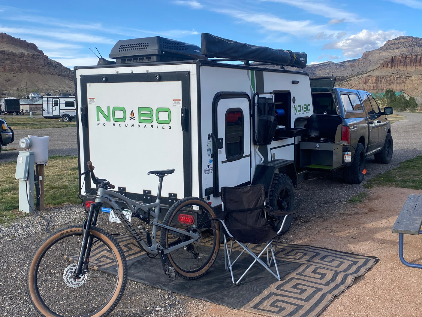 Off-road RV rental setup at a scenic campsite with a pickup truck and mountain bike, ready for adventure.