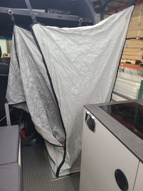 Inside an RV rental, a crinkled light gray privacy curtain creates a private space next to a compact kitchenette with a stovetop.