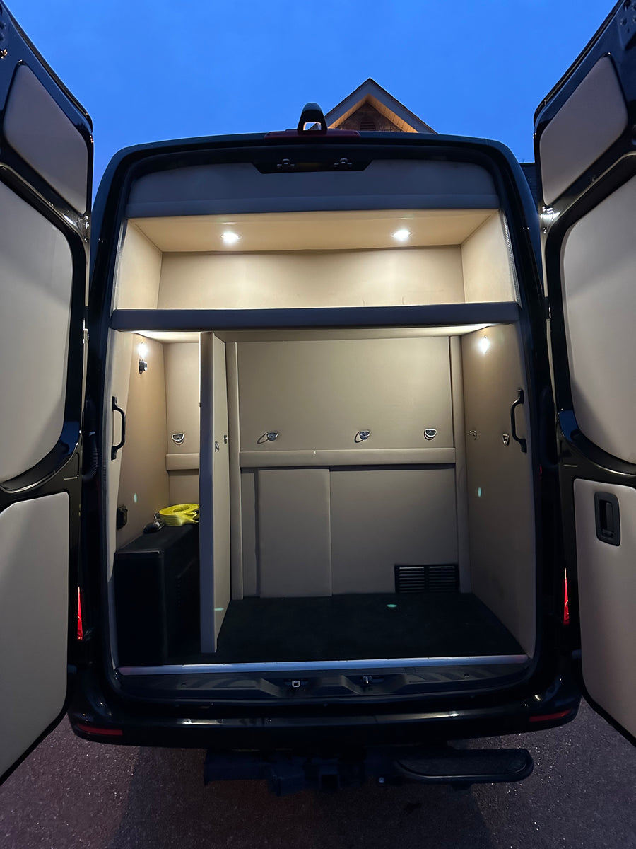 Rear interior of a custom rv rental van, featuring illuminated shelves, padded walls, and a spacious cargo area for gear.