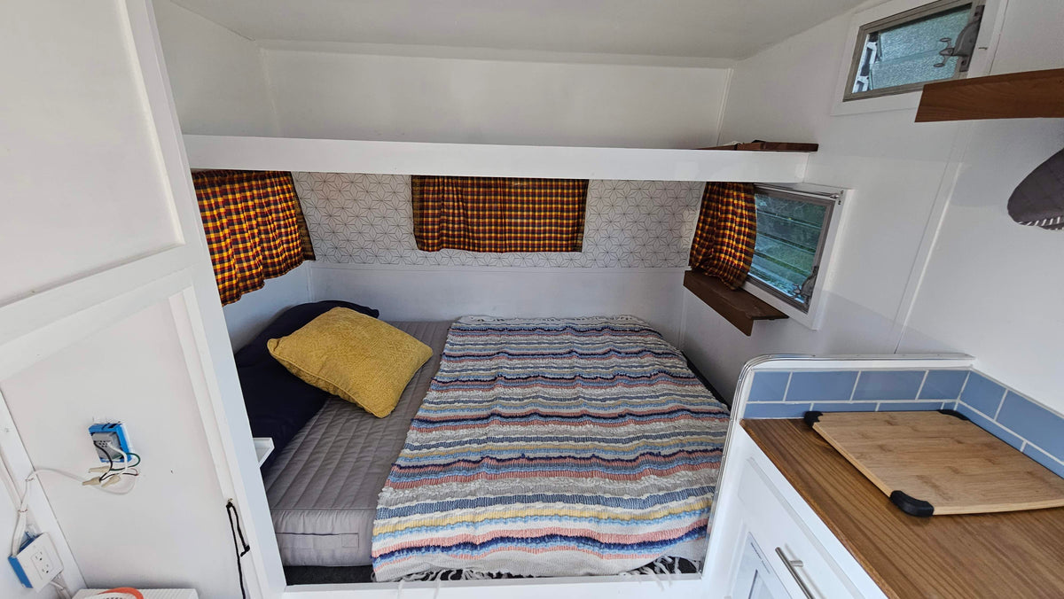 Inside a compact RV rental: a bed with striped blanket, plaid curtains, and a small kitchenette area. — photo 7
