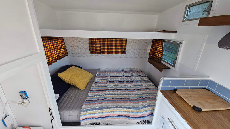 Inside a compact RV rental: a bed with striped blanket, plaid curtains, and a small kitchenette area. — photo 7
