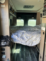 Inside an RV rental: a comfy bed awaits, with climate control, utility panels, and floor tracks for gear.