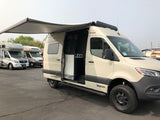 Tan Winnebago camper van with awning out, an ideal RV rental for adventure. Other RVs visible.
