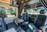 Modern RV rental interior with front swivel seats, digital control panel, and dining/work table, offering a comfortable adventure.