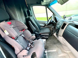 View inside an RV rental van showing a child seat, driver's cockpit, and dark privacy curtains.