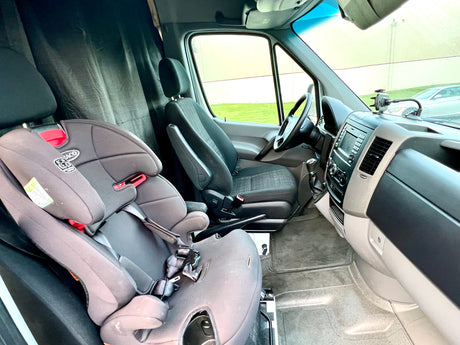 View inside an RV rental van showing a child seat, driver's cockpit, and dark privacy curtains.