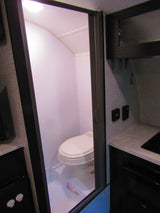 RV rental interior: a small, functional bathroom with a toilet and shower pan, next to a compact kitchen area.