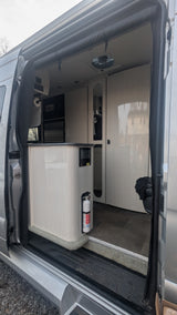 Interior of an rv rental camper van, showing a functional kitchen with cabinets, microwave, and a fire extinguisher.
