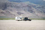 Adventure awaits! An SUV tows a sleek travel trailer on a vast plain, framed by mountains. Ideal for an RV rental getaway.