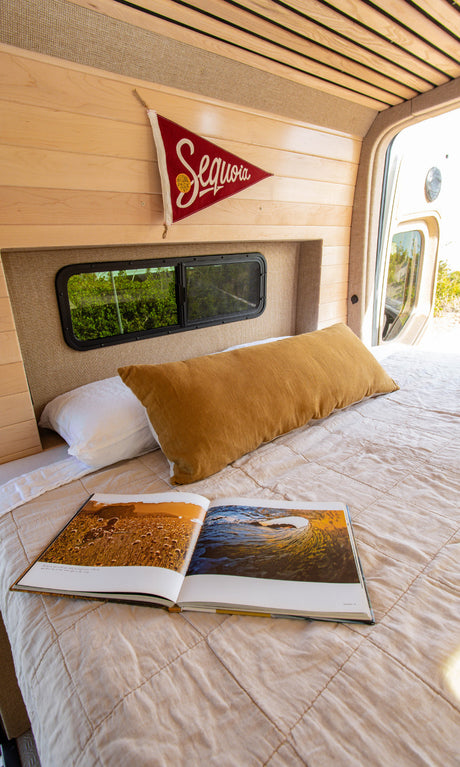Relax in your RV rental's comfy bed! This camper van boasts wood paneling, a view window, and reading space.