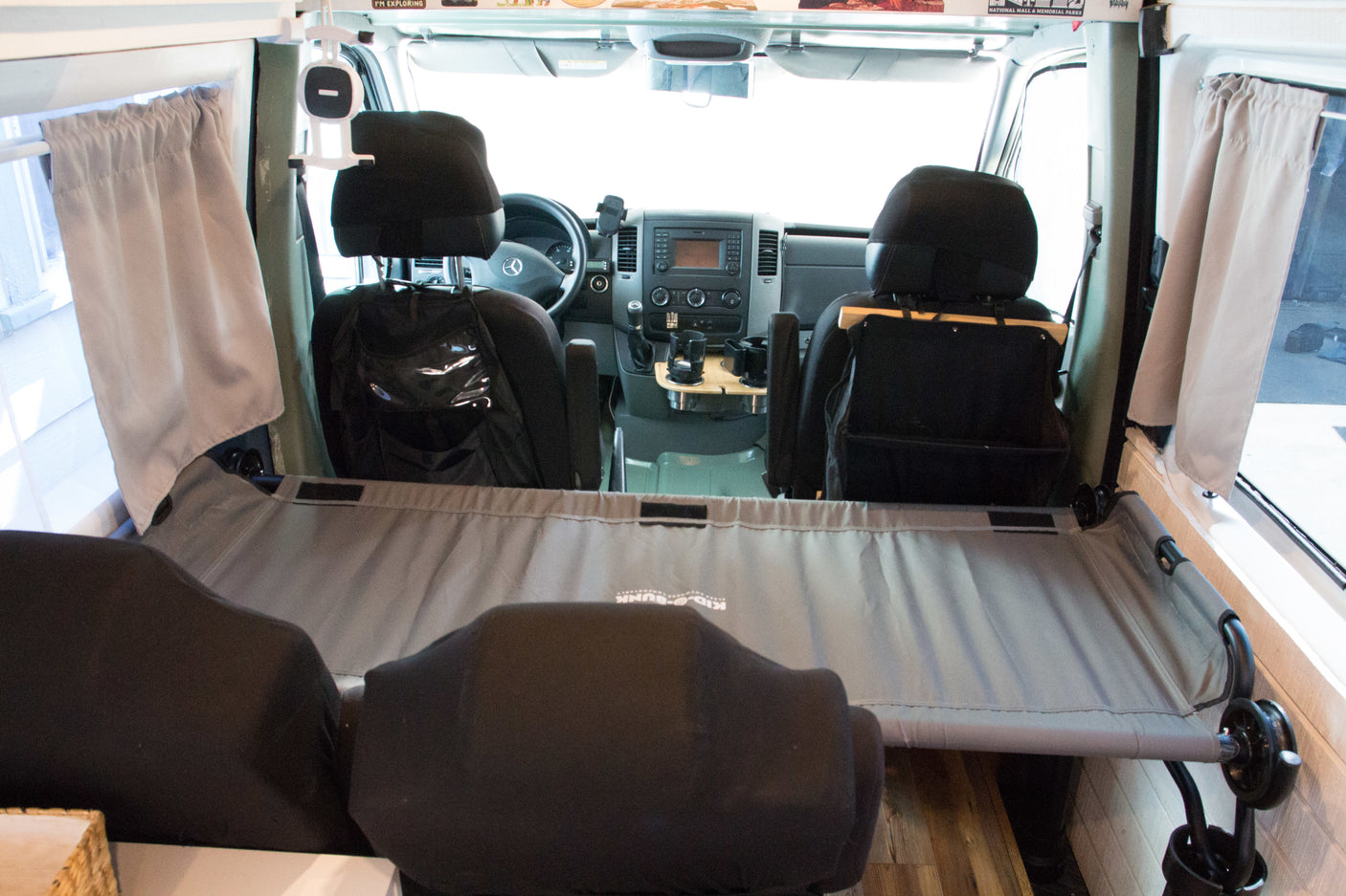 Inside an rv rental van, showing the front cockpit area, driver's seat, and a gray bunk bed system across the middle.
