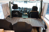 Inside an rv rental van, showing the front cockpit area, driver's seat, and a gray bunk bed system across the middle.