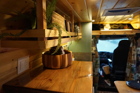 Inside a cozy RV rental: wooden interior, shelves with plants, and a clean kitchen counter leading to the driver's cab.