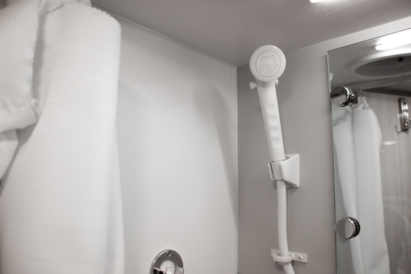 Clean shower amenities in an RV rental. Handheld showerhead, mirror, and white towel/robe offer comfort.