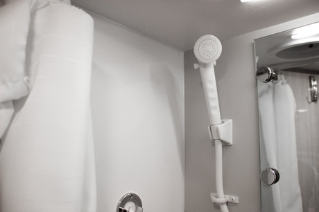 Clean shower amenities in an RV rental. Handheld showerhead, mirror, and white towel/robe offer comfort.