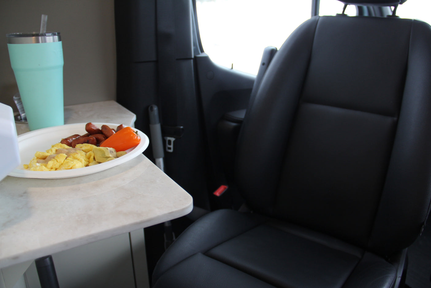 Breakfast in an RV rental: scrambled eggs, sausages, and bell pepper on a counter, with a tumbler and vehicle seat visible.
