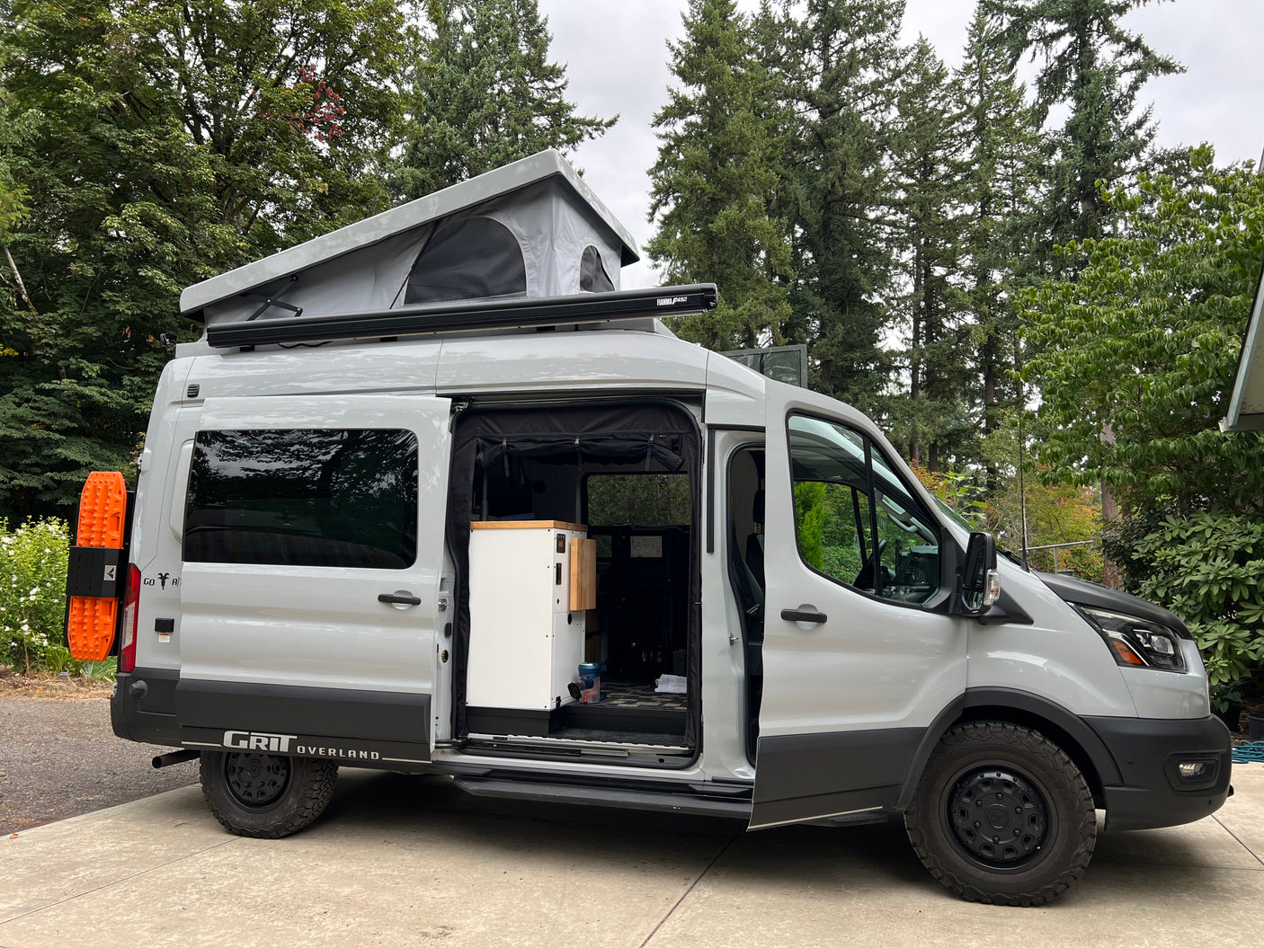 Spacious Ford Transit pop-top camper van, equipped for overland RV rental trips, with open side door revealing interior.