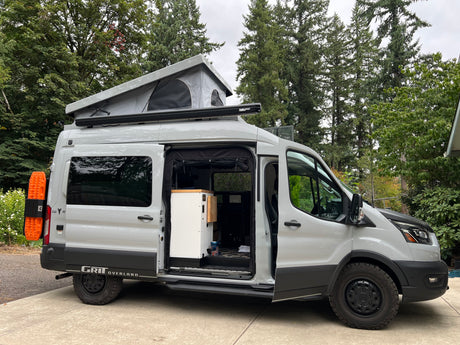 Spacious Ford Transit pop-top camper van, equipped for overland RV rental trips, with open side door revealing interior.
