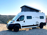 White pop-top Rove Vans camper van for rv rental, parked on a gravel path in a desert landscape.