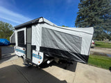 This white and black pop-up camper, a great RV rental option, is set up on a sunny driveway.