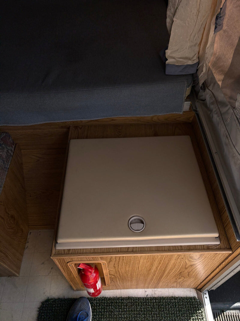 Inside an RV rental: a compact bed/seating area, a functional table, and a fire extinguisher for safety. — photo 6