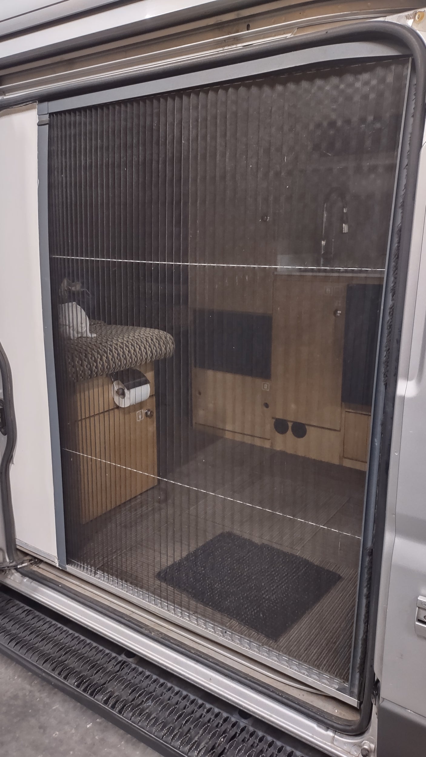 RV rental: View through a pleated window blind into the RV's interior, showing wooden cabinets and furnishings.
