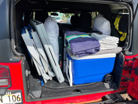 Red Jeep loaded for adventure! Camping gear, cooler, & chairs packed, ideal for your RV rental getaway.