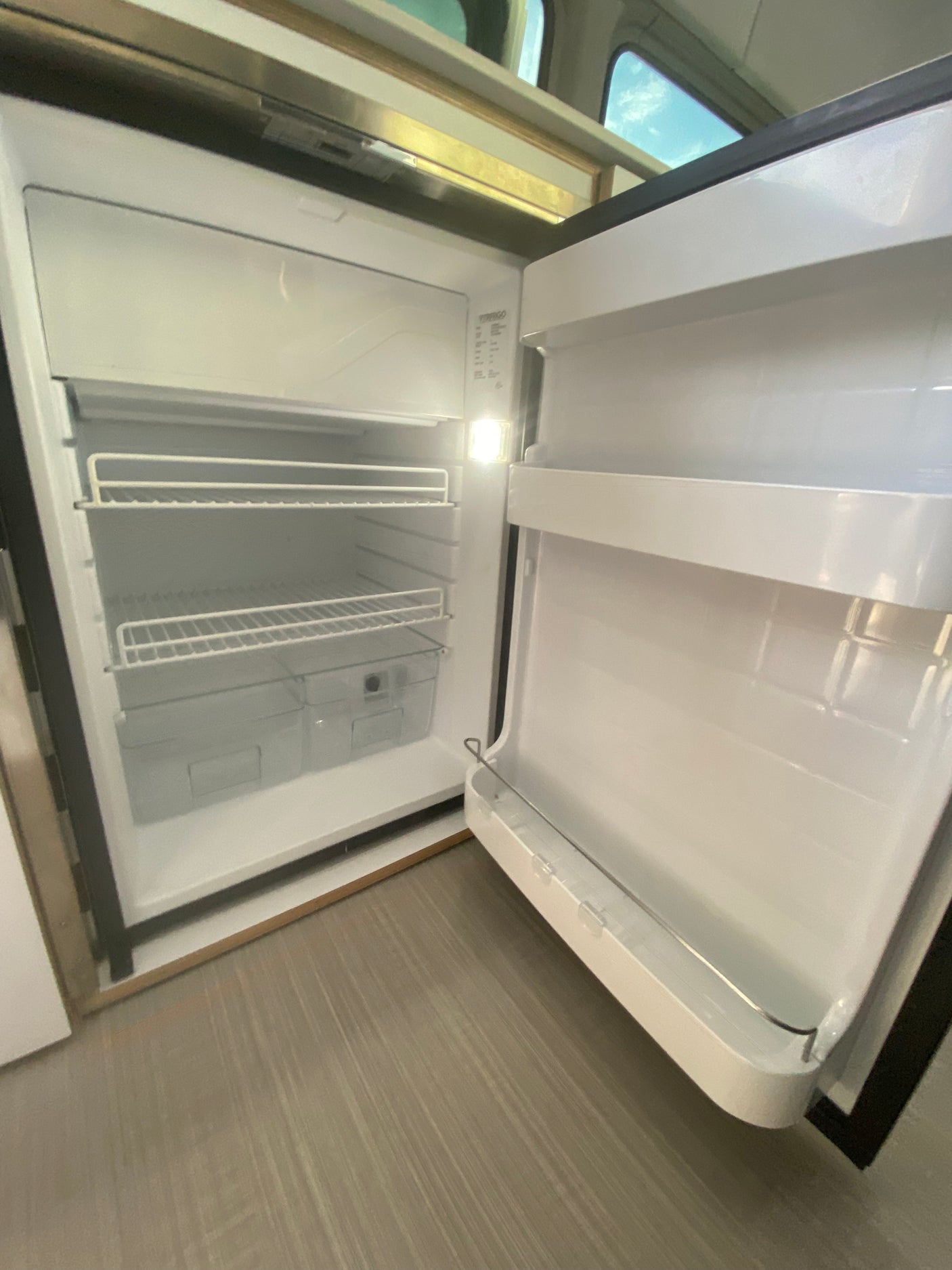 An open, clean RV rental refrigerator with shelves and crisper, ready for your travel provisions.