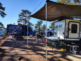 Sunny rv rental campsite: A white No Boundaries camper and a blue Micro Minnie are set up with an awning, tables, and a dog.