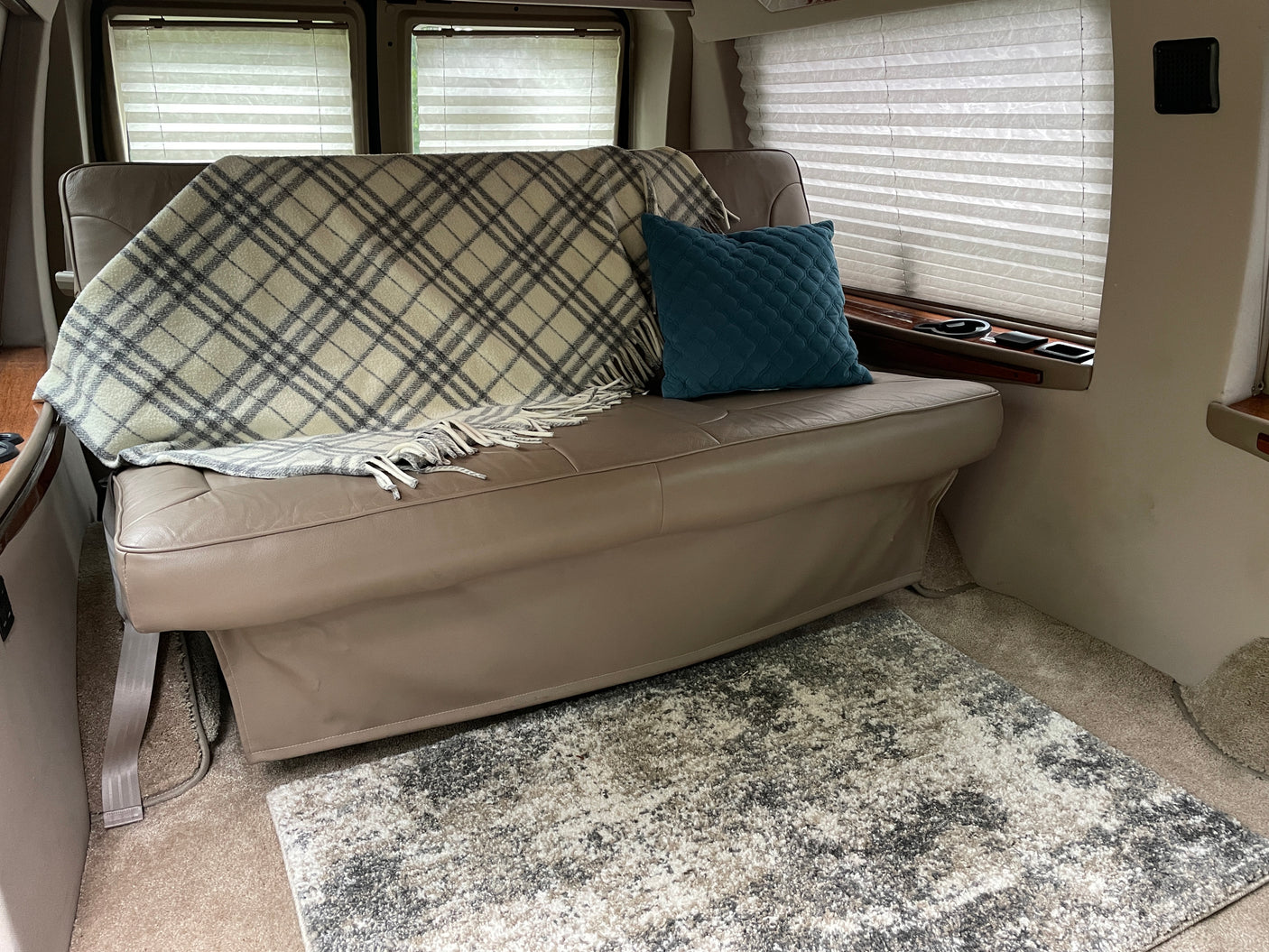 Cozy RV rental interior featuring a comfortable bench seat, plaid blanket, teal pillow, and soft rug.