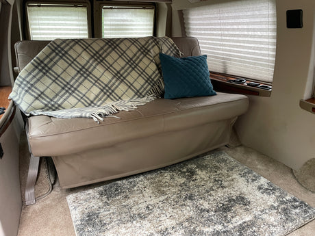 Cozy RV rental interior featuring a comfortable bench seat, plaid blanket, teal pillow, and soft rug.
