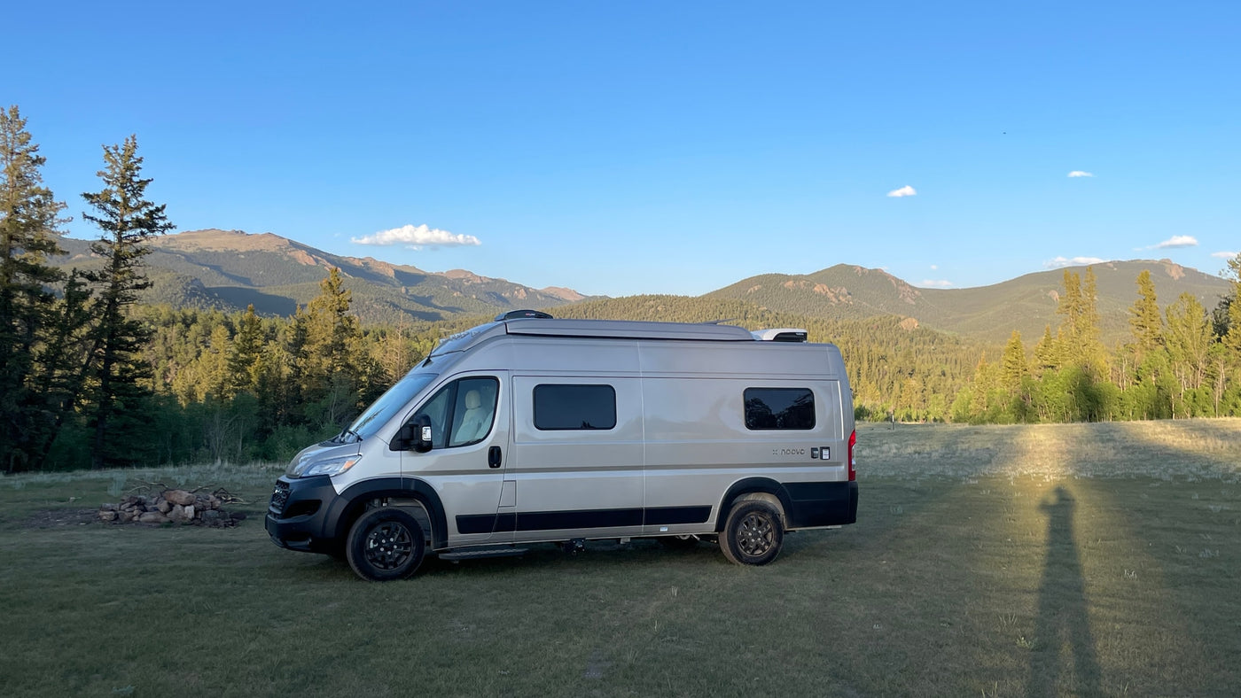 An RV rental camper van is parked in a grassy mountain field, surrounded by forests under a clear blue sky. — photo 17
