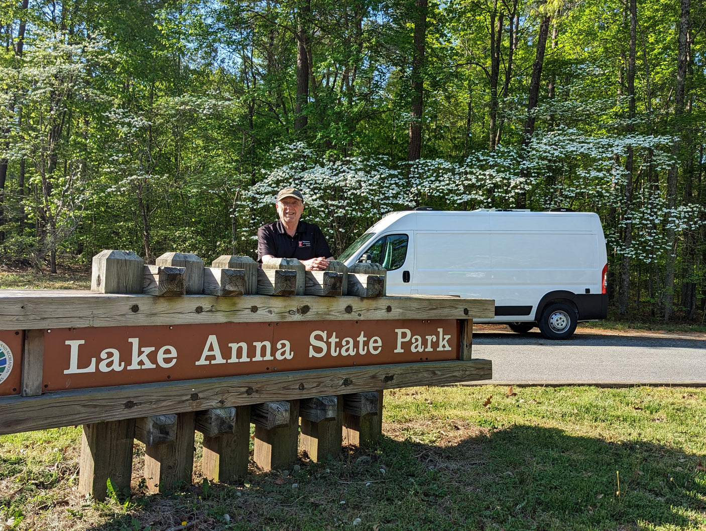 A man and his white RV rental van at Lake Anna State Park, with blooming dogwood trees in the background.