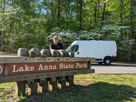 A man and his white RV rental van at Lake Anna State Park, with blooming dogwood trees in the background.
