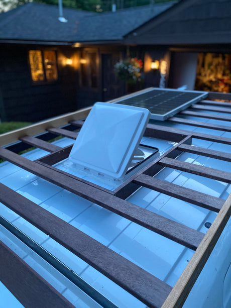 Top view of an RV rental roof with an open vent, solar panel, and custom wood roof rack.