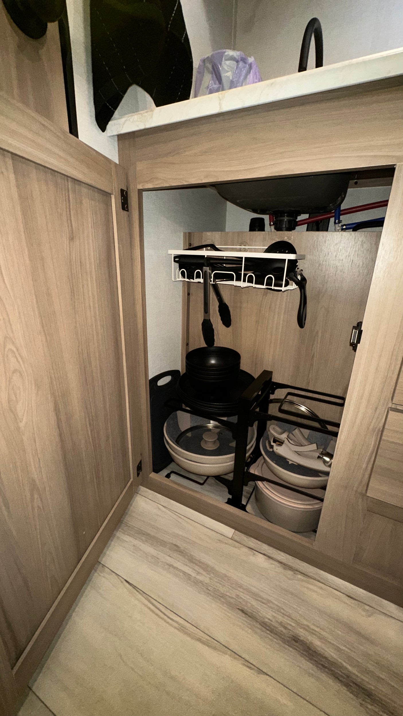 Efficient under-sink storage in an RV rental kitchen, showing organized pots, pans, and utensils.