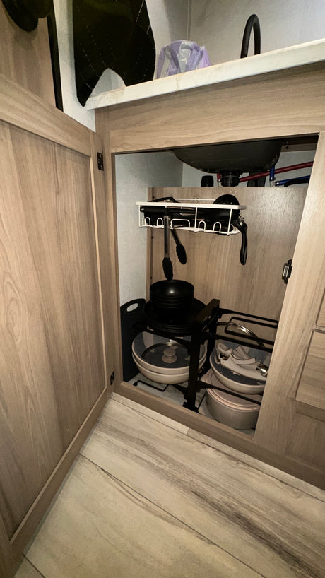 Efficient under-sink storage in an RV rental kitchen, showing organized pots, pans, and utensils.