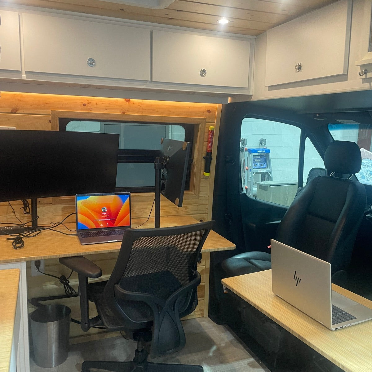 This RV rental offers a mobile office setup with dual monitors, two laptops, and an ergonomic chair within a custom-built van.