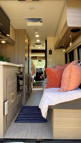 Cozy RV rental interior with light wood cabinetry, a comfortable bed, compact kitchen area, and view to the front cabin.